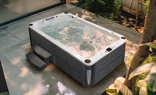 An overhead view of a Cal Spas Deck hot tub with blue corner lights and 30-inch steps on a wooden, wooded patio.